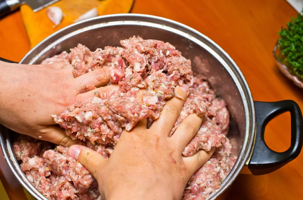 Close up of hands mixing up sausage meat in a bowl.